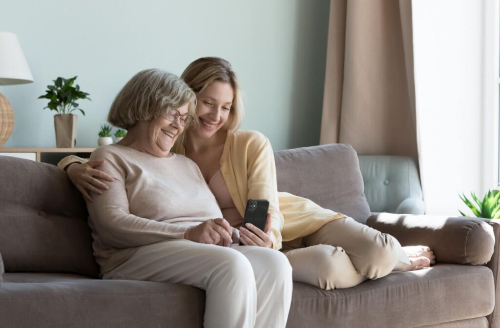 A senior and their adult child sit on a couch looking at a phone
