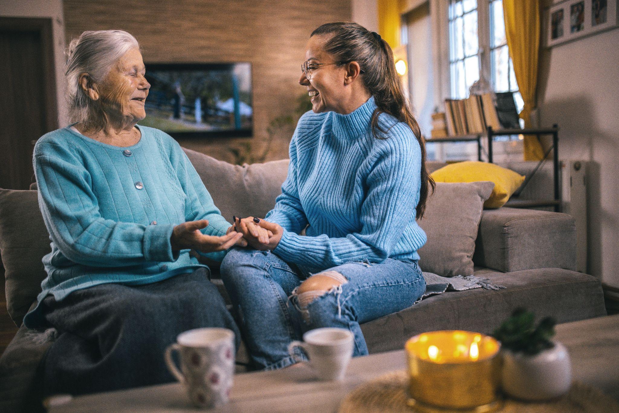 An elderly woman and an older adult talk to each other over a cup of tea.